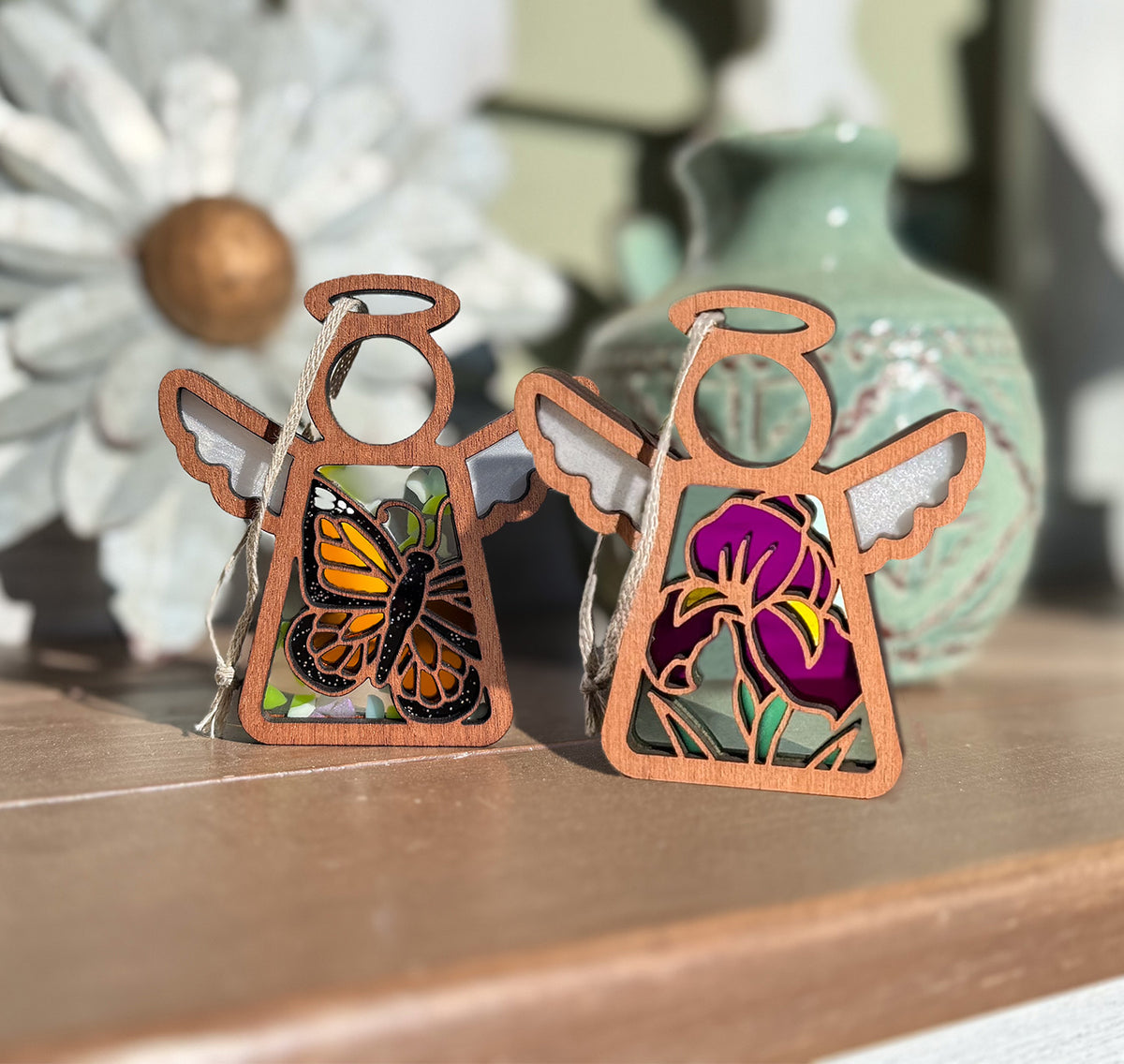 Two angel-shaped decorative pieces with butterfly and flower designs on a wooden surface.