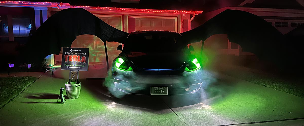 Tesla Model 3 dressed as Toothless the dragon from How to Train Your Dragon with glowing green headlights on a dark driveway on Halloween night