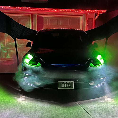Tesla Model 3 dressed as Toothless the dragon from How to Train Your Dragon with glowing green headlights on a dark driveway on Halloween night