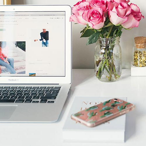Laptop on a desk with a vase of pink flowers, phone, and other items.