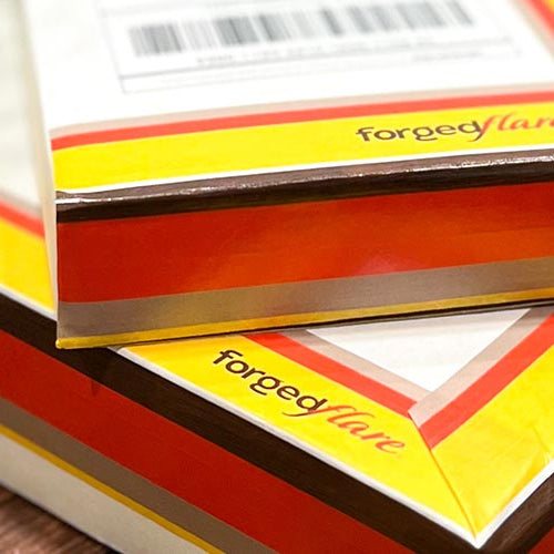 Two packaged boxes of Forged Flare ornaments on a wooden background.