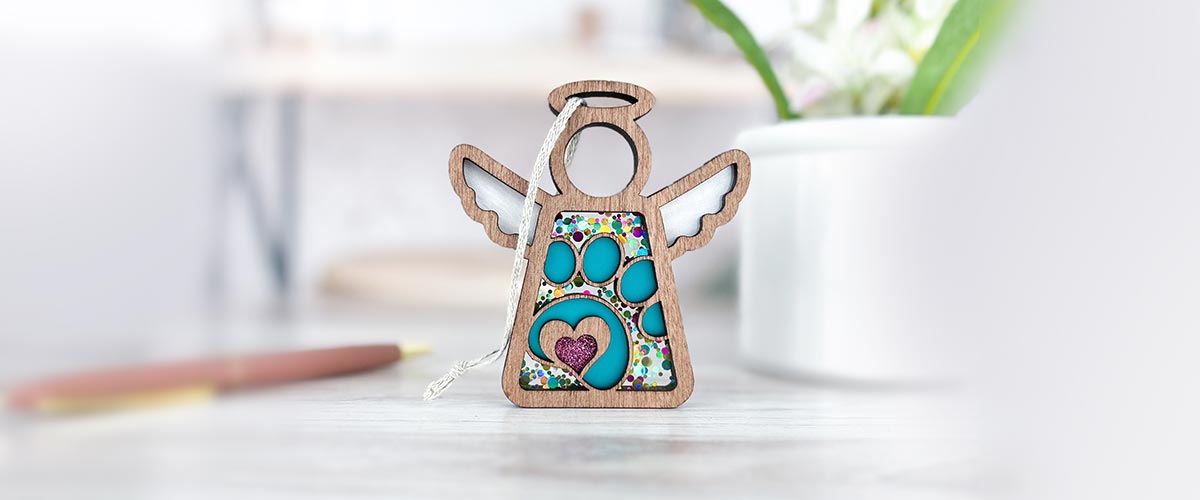 Forged Flare® rainbow bridge gift, a wooden Mother’s Angels® paw print angel ornament with colorful design, displayed on a white surface to honor your pet.