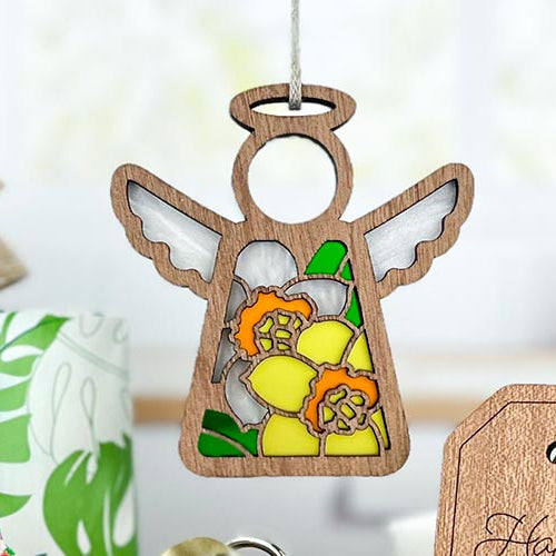 Wooden angel ornament with floral daffodil birth flower design on a blurred background.