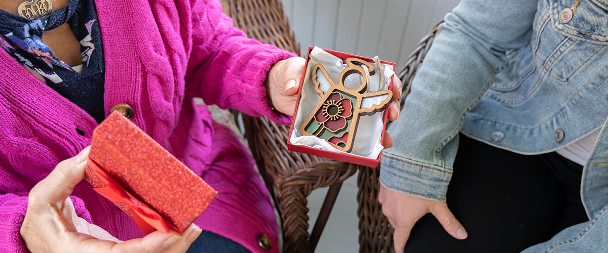 Two people holding red gift boxes with decorative items, one in a pink sweater and the other in a denim jacket.