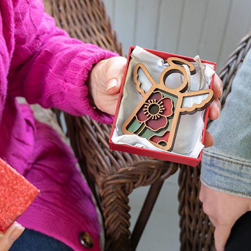Two people holding red gift boxes with decorative items, one in a pink sweater and the other in a denim jacket.