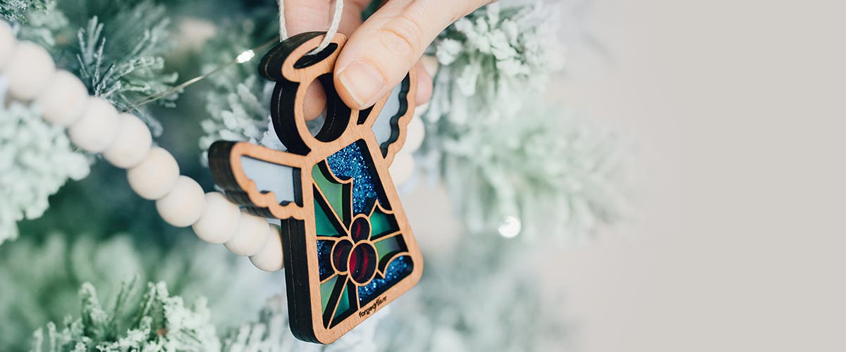 Decorative Christmas ornament with stained glass inspired holly berries design held against a Christmas tree.