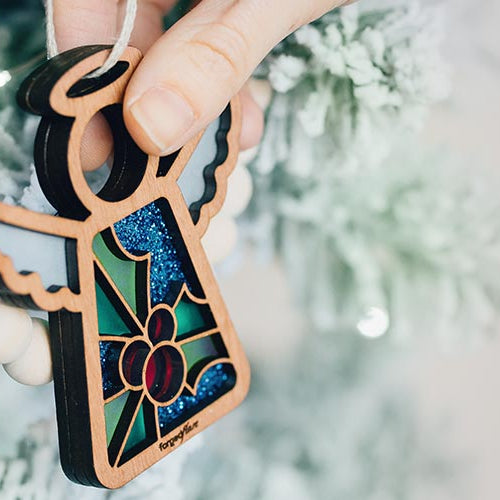 Decorative Christmas ornament with stained glass inspired holly berries design held against a Christmas tree.