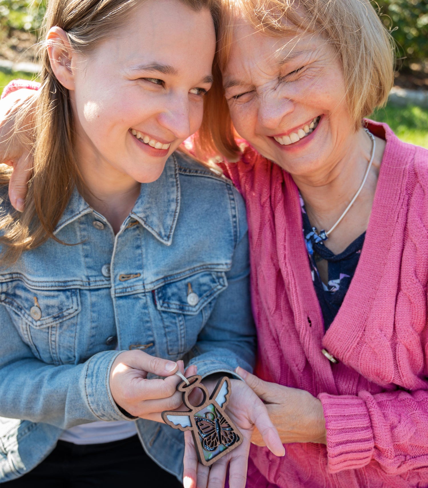 Daughter and her mother smiling and laughing while holding a monarch butterfly Mother’s Angels ornament.