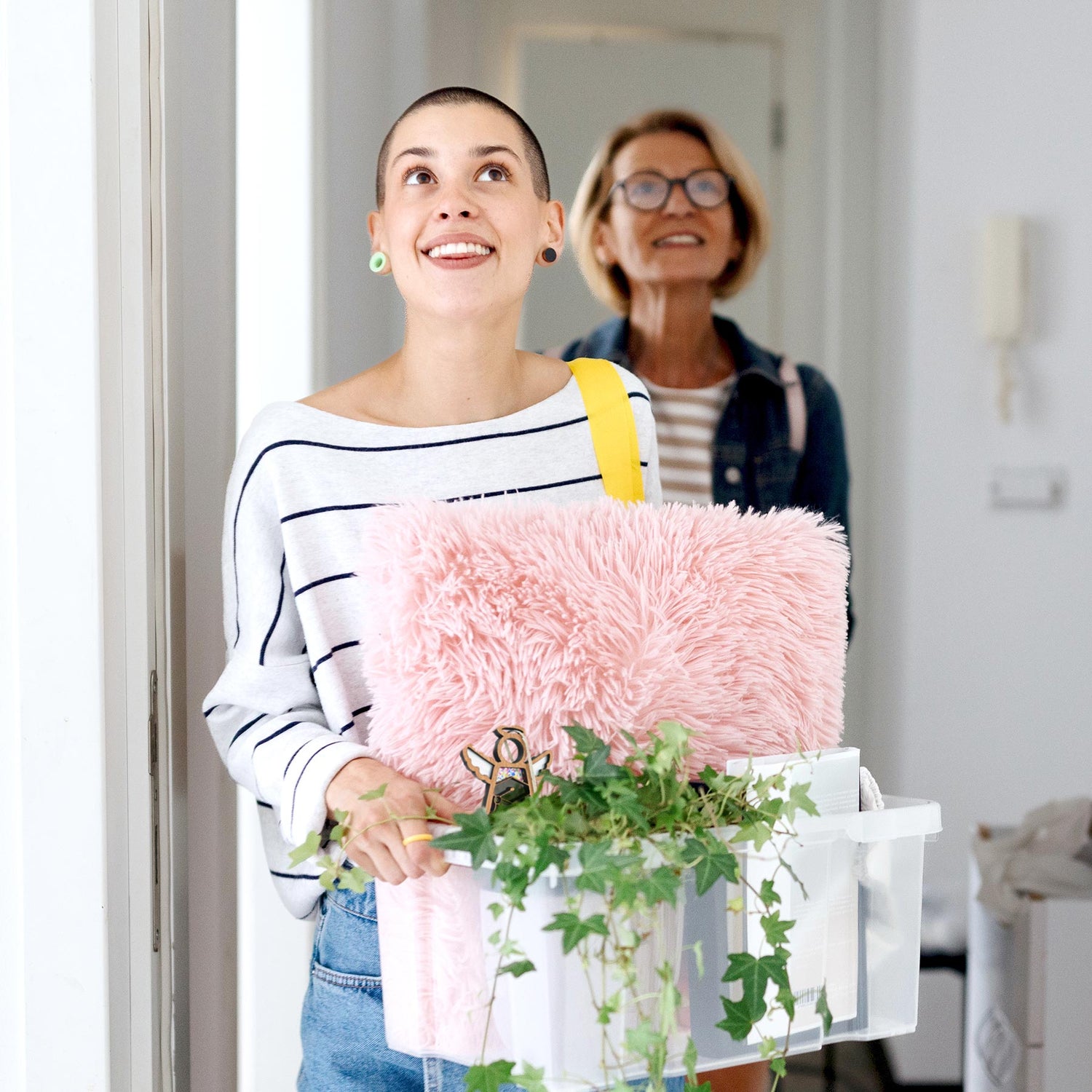 A cheerful daughter moving into her college dorm, snuggling a Mother’s Angels® Graduation ornament among her items, symbolizing a cherished graduation gift. Her mother looks on with pride, the perfect representation of a memorable graduation present for her.