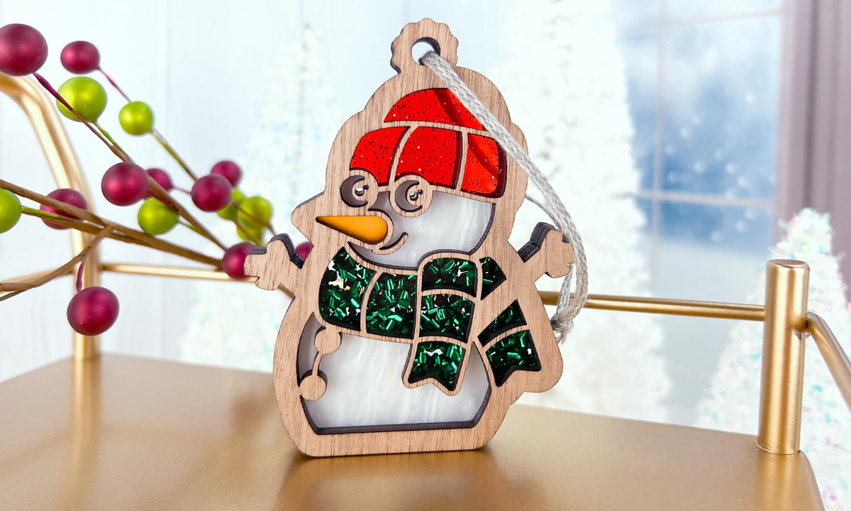 Wooden snowman ornament with a red hat and green scarf on a decorative stand.