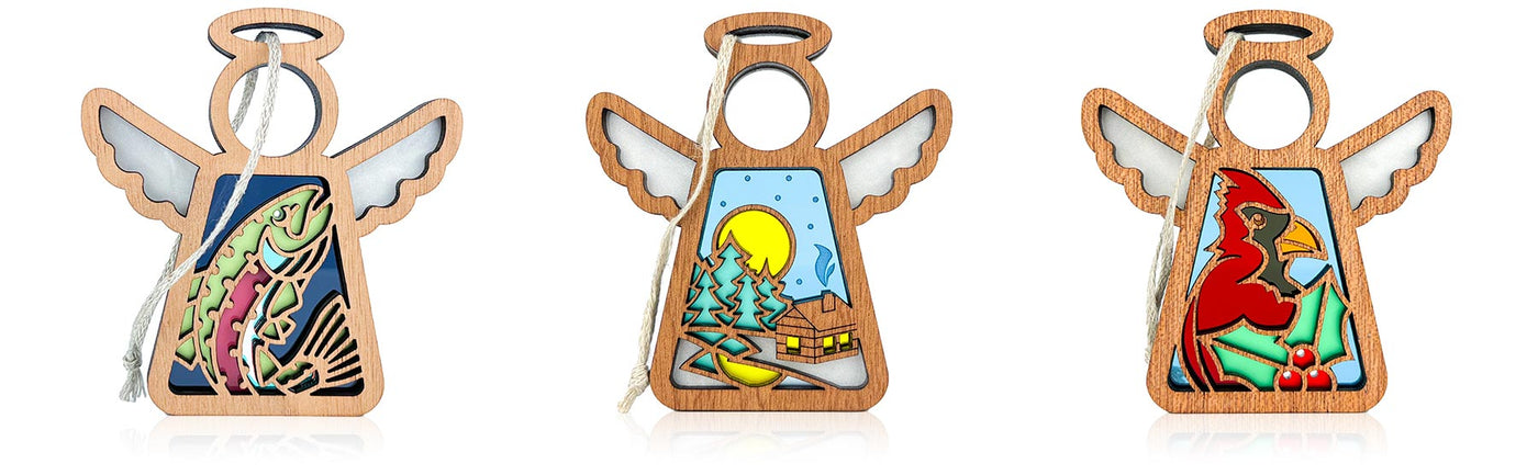 Three angel ornaments with different designs on a white background. The first shows a rainbow trout on a navy background, the second is of a snowy scene with a cozy Christmas cottage set in a peaceful forest, and the third shows a red cardinal with holly leaves and berries.