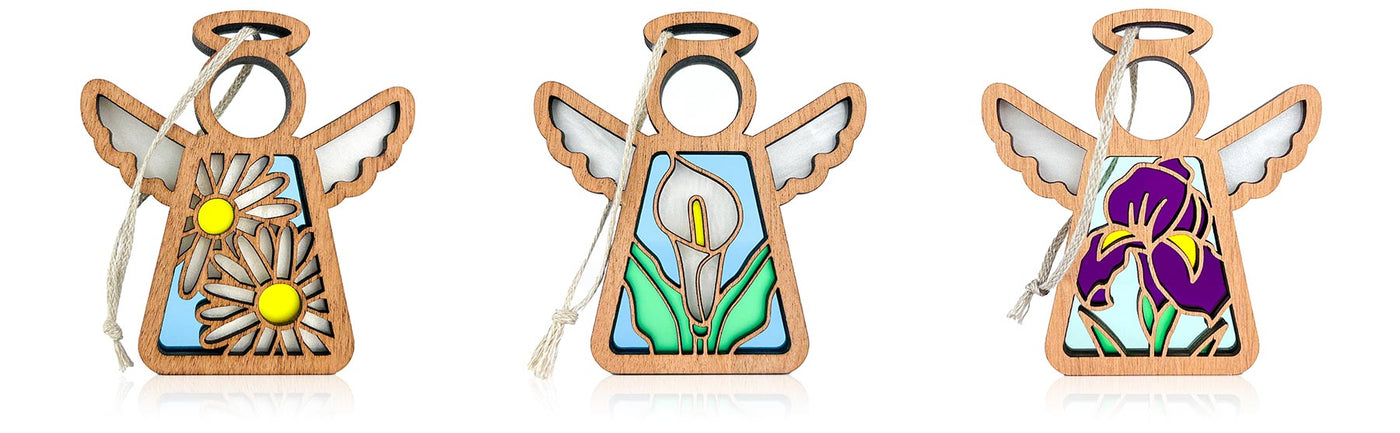 Three angel ornaments with floral designs on a white background. The first angel ornament showcases two white daisies on a blue background, the second shows a white calla lily flower with green leaves on a light blue background, and the third shows a vibrant purple iris flower on a light blue background.