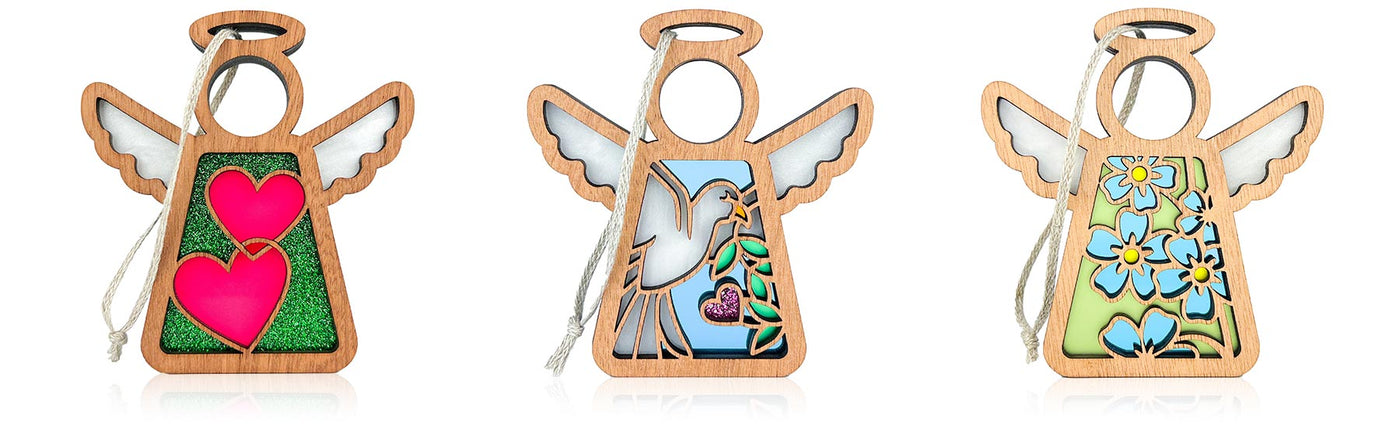 Three wooden angel ornaments with colorful designs on a white background. The first shows interlocking hot pink hearts against a glittery green background. The second design shows a flying dove carrying a peace branch and heart flower. The third design shows a bunch of blue forget-me-not flowers against a light green background.