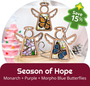 Two wooden Mother's Angels® 3.5" angel figurines (Daisy, Sunflower) by Forged Flare® from the Holiday Cheer 2-Piece Bundle are displayed with a "Save 15%" holiday sale tag, festive decor, and a blurred pink Christmas tree in the background.