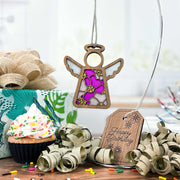 The Forged Flare® Primrose Ornament, a 3.5" angel figurine from Mother's Angels®, with pink and gold accents, floats above a birthday setup featuring gifts, a cupcake, and confetti—highlighting the pink primrose birth flower.