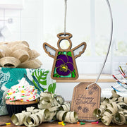A Forged Flare® Violet Ornament | 3.5" Angel Figurine from Mother's Angels® hangs above a sprinkled cupcake, wrapped gift, curled ribbon, and a “Happy Birthday” tag on a table in a bright kitchen.