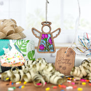 A Forged Flare® Sweet Pea Ornament, a 3.5" Mother's Angels® angel figurine with a stained-glass center, hangs with birthday decor—wrapped gift, curled ribbons, Happy Birthday tag, and sweet pea flower accents for a special touch.