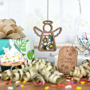 A Forged Flare® Hawthorn Ornament | 3.5" (H) Angel Figurine from Mother's Angels® hangs near a sprinkle-topped cupcake, “Happy Birthday” tag, ribbon, confetti, and a floral gift box in this festive birth flower scene.