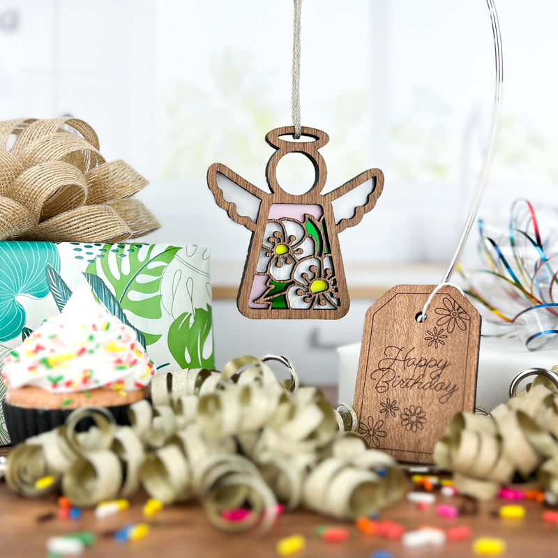 A Forged Flare® Hawthorn Ornament | 3.5" (H) Angel Figurine from Mother's Angels® hangs near a sprinkle-topped cupcake, “Happy Birthday” tag, ribbon, confetti, and a floral gift box in this festive birth flower scene.