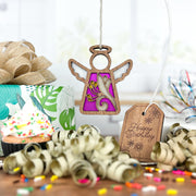 A Forged Flare® Honeysuckle Ornament (3.5" angel figurine from Mother's Angels®), featuring purple and gold, hangs above a sprinkle-topped cupcake. A birth flower tag, curling ribbon, confetti, and gift box add birthday cheer.