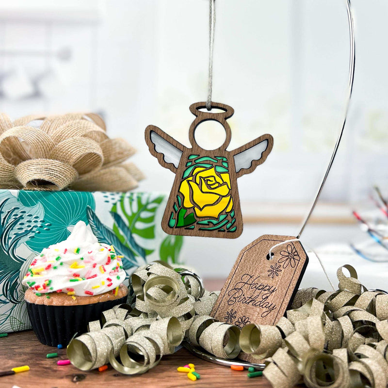 A birthday scene with a beautifully wrapped present, a cupcake with white frosting and colorful sprinkles, and a Yellow Rose Ornament 3.5" Angel Figurine from the Mother's Angels® collection by Forged Flare®. Gold ribbon curls and a "Happy Birthday" tag add to the festive atmosphere.