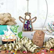 The Forged Flare® Mother's Angels® Larkspur Ornament—a 3.5" wooden angel with a colorful larkspur floral design for July birthdays—hangs above a cheerful scene with a cupcake, gifts, gold ribbon, and "Happy Birthday" tag.