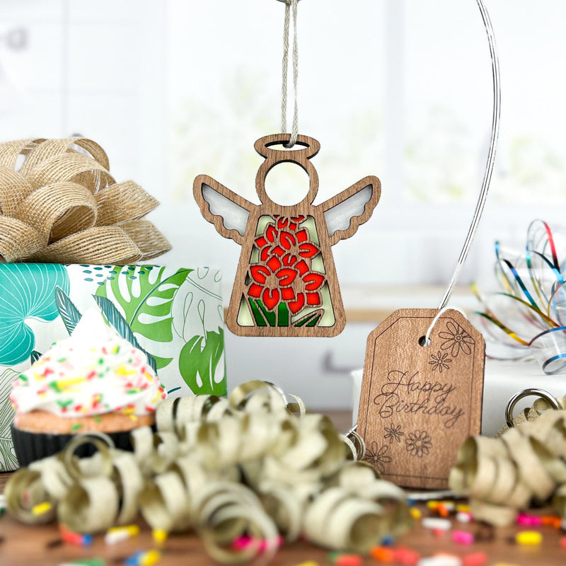 A Forged Flare® Gladiolus Ornament | 3.5" Angel Figurine from Mother's Angels® hangs among birthday décor—sprinkled cupcake, floral-wrapped gift, curly ribbons, and a wooden “Happy Birthday” tag.