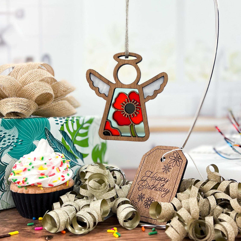The Forged Flare® Mother's Angels® Poppy Ornament (3.5" angel figurine) from Amazon adds a festive touch above a birthday scene with a cupcake, gold ribbon, gift box, and "Happy Birthday" tag—ideal for special celebrations.