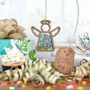 A Forged Flare® Mother's Angels® Morning Glory Ornament (3.5" angel figurine) hangs by a "Happy Birthday" tag near a sprinkle cupcake, wrapped gift, ribbon curls, and confetti on the table.