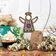 A Forged Flare® Mother's Angels® Chrysanthemum Ornament with imperfections hangs near a sprinkled cupcake, golden ribbon curls, and a "Happy Birthday" tag on the kitchen counter.