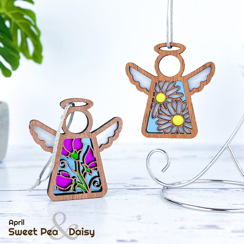 Two Forged Flare® Mother's Angels® warehouse return ornaments—each 3.5" tall with stained-glass wings—feature floral dresses, one with purple flowers and one with white daisies. Available on the Amazon marketplace.