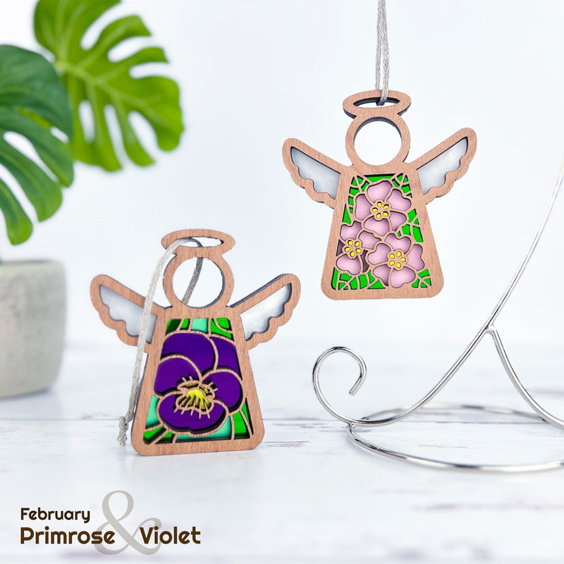 The Forged Flare® Pink Evening Primrose Ornament is a 3.5" Mother's Angels® figurine with stained-glass-style wings and floral design celebrating February’s birth flower. "February Primrose & Violet" appears next to a leafy plant.