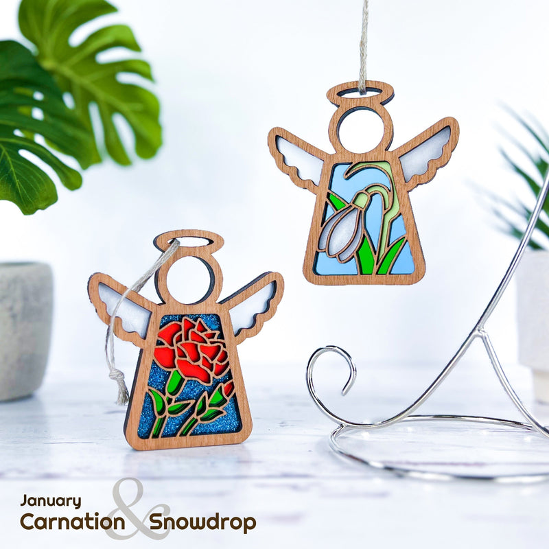 Two Forged Flare® Mother's Angels® Carnation Ornaments (3.5"H), each with a birth flower—one stained-glass carnation, the other snowdrops—hang by a plant and stand. Text: “January Carnation & Snowdrop.”.