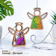 Two Forged Flare® Mother's Angels® ornaments, each 3.5" tall, display October birth flowers—cosmos and marigold. Both wooden angels hang by string among green leaves on a metal stand. Text reads "October Cosmos & Marigold.