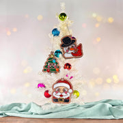 Santa, snowman with cardinal, and Christmas tree ornaments hanging on a small white Christmas tree with colorful baubles