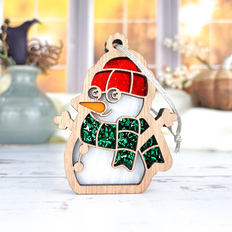 The Forged Flare® Christmas Snowman Ornament, 3.6" tall, features a red hat, green glittery scarf, and orange carrot nose, hanging by a white string—perfect festive décor for your tree or display this holiday season.
