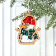 The Forged Flare® Christmas Snowman Ornament, 3.6" tall with a red hat, green and blue scarf, and glasses, hangs from a pine branch—ideal as a festive decoration or thoughtful snowman gift.