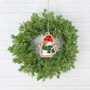 A Forged Flare® Christmas Snowman Ornament, 3.6" (H), with a red hat and green scarf, decorates a green holiday wreath on a white brick wall—an ideal festive accent for your home.