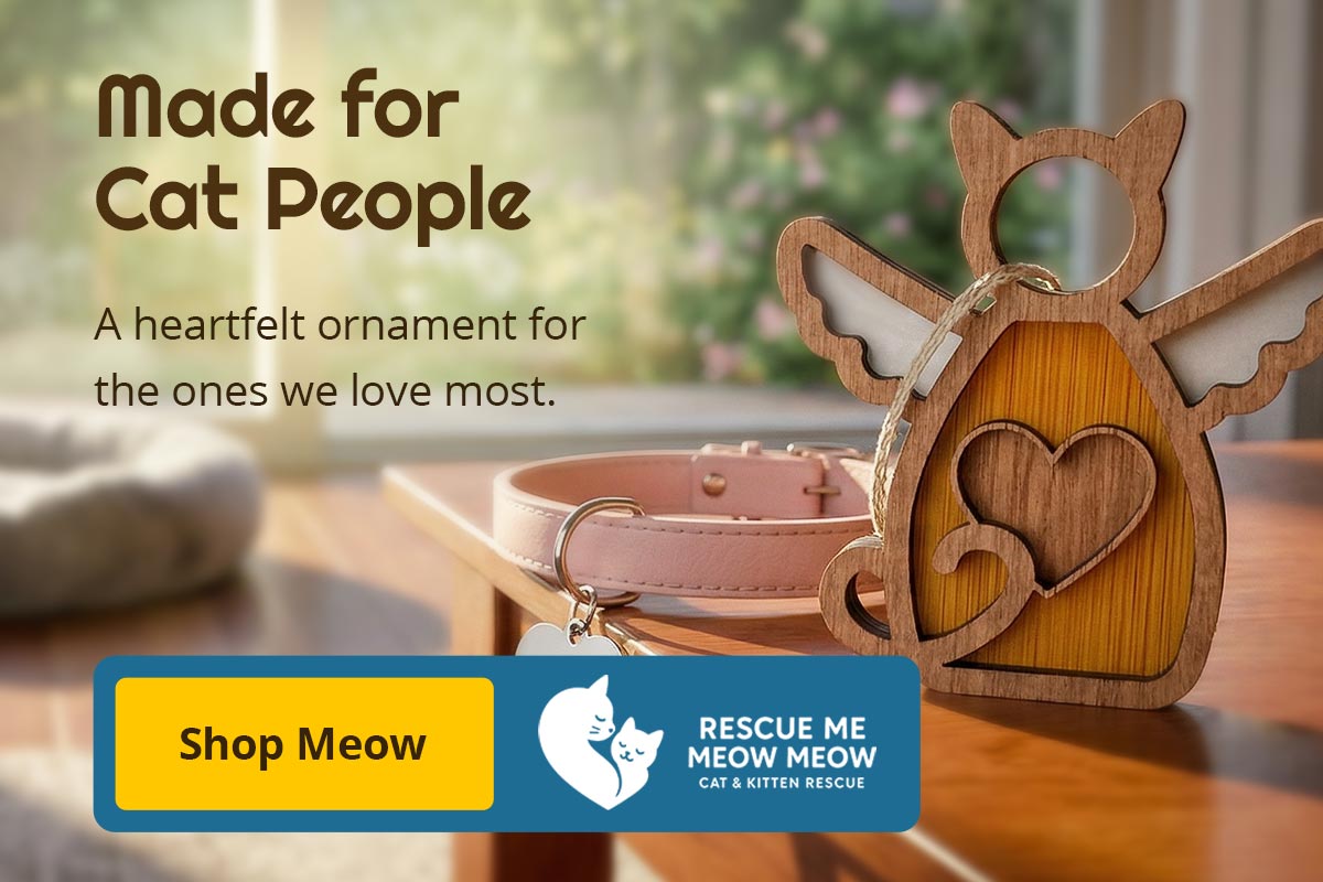 Decorative cat ornament with heart design on a wooden surface, with a blurred background of a cat bed and window. Text reads: Made for Cat People. A heartfelt ornament for the ones we love most. Shop Meow. Proceeds benefit Rescue Me Meow Meow Cat & Kitten Rescue