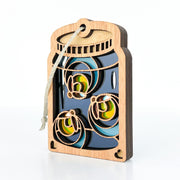 The Forged Flare® Fireflies Jar Ornament, 3.6" (H), features layered wooden cutouts of three fireflies with colorful wings inside a mason jar shape, and includes an attached hanging string. The background is plain white.