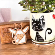 The Forged Flare® Forever Loved Cat Angel Ornament for Charity features a winged cat with a heart reading "Coconut," placed before a ceramic pot with a black cat and leafy plant—a perfect personalized pet ornament or memorial.