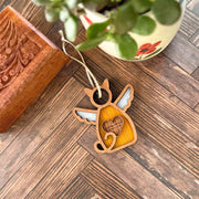 The Forged Flare® Forever Loved Cat Angel Ornament for Charity is a wooden cat-shaped memorial with wings and a heart cutout inscribed "You were my favorite hello and my hardest goodbye," shown beside a potted plant and carved wooden box.