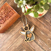 A Forged Flare® Forever Loved Cat Angel Ornament for Charity lies on a wooden floor next to a carved box, potted succulent, and engraved "Mommy" angel-shaped ornament.