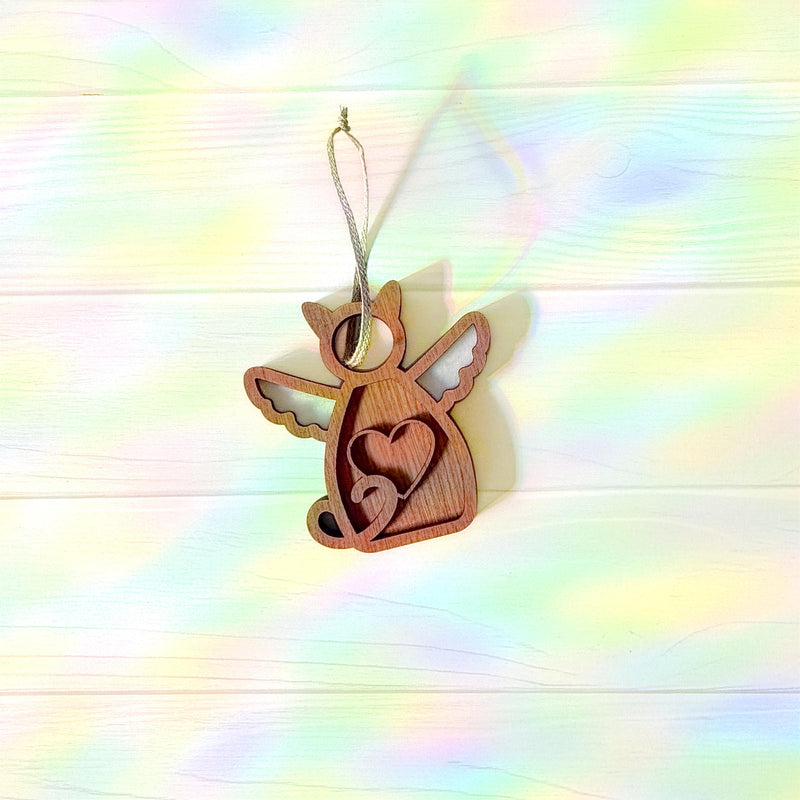 The Forged Flare® Forever Loved Cat Angel Ornament for Charity features a wooden angel with wings and a heart cutout, hanging on a string against a pale, rainbow backdrop—an ideal keepsake to honor your cat’s memory.