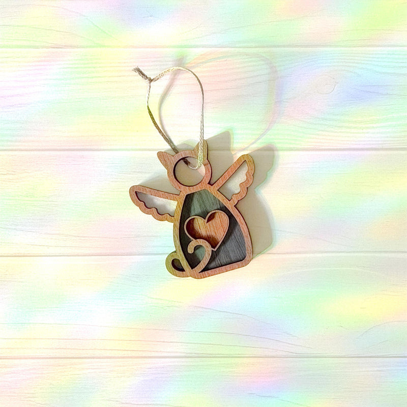 The Forged Flare® Forever Loved Cat Angel Ornament for Charity features a winged cat with a heart cutout, hanging from a string on a pastel rainbow wooden background—perfect as a personalized pet ornament or heartfelt cat memorial.