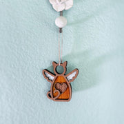 The Forged Flare® Forever Loved Cat Angel Ornament for Charity, featuring wings and a heart cutout, hangs from a string on a white bead and rose hook against a light blue textured wall.