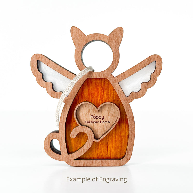 The Forever Loved Cat Angel Ornament for Charity by Forged Flare® is a wooden ornament with angel wings, cat tail, and heart engraved "Poppy Furever Home," plus a rope loop. Text below reads "Example of Engraving.