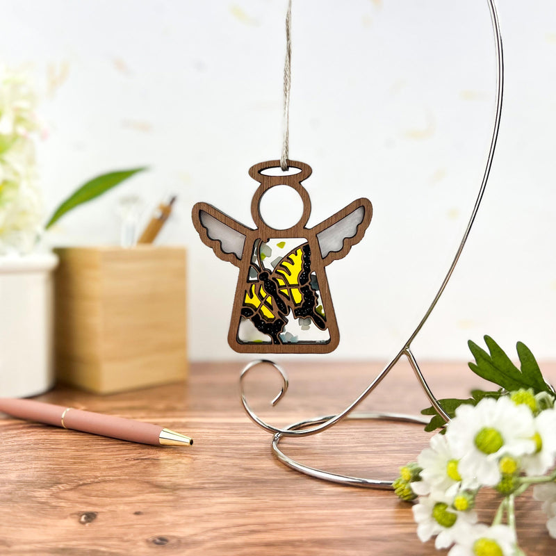 The Warehouse Return Swallowtail Butterfly Ornament (3.5" H) Mother’s Angels® by Forged Flare® features a yellow and black butterfly angel, perfect as a gift or unique Amazon find, displayed on a metal stand among office decor.
