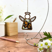 The Forged Flare® Monarch Butterfly Ornament with Imperfections, a 3.5" stained glass-style Mother's Angels® angel figurine, hangs on a metal stand—perfect as a memorial keepsake or touching gift.