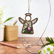 The Forged Flare® Cabbage Butterfly with Clover Flower Ornament is a 3.5" Mother's Angels® figurine, adding charm to any space—perfect for angel lovers. A pen, flowers, and a white pot appear softly blurred in the background.